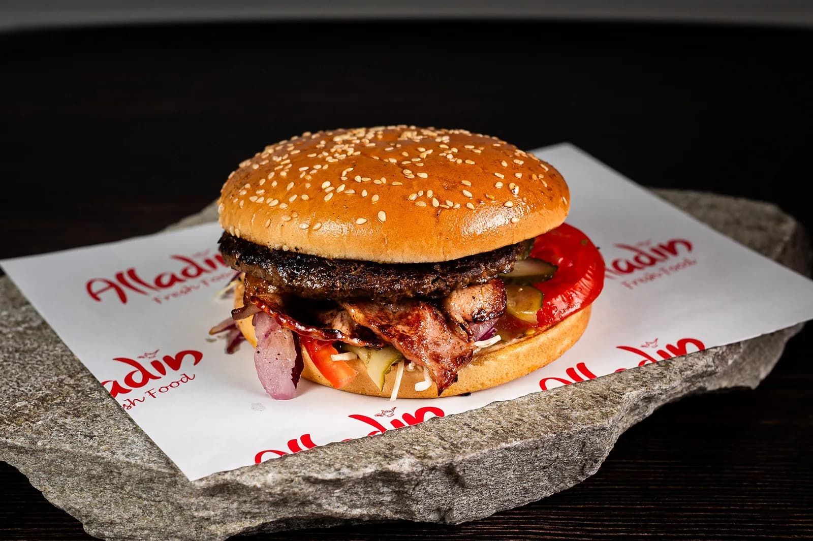 Bacon Burger fotografiat frontal, cu carne de vită, bacon, roșii și ceapă roșie, pe hârtia brandată Alladin